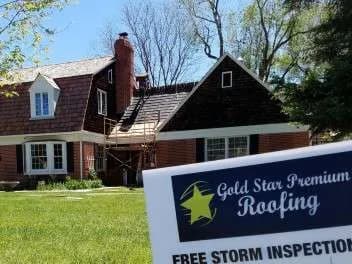 Brick house with roof work underway and a Gold Star Premium Roofing yard sign offering free storm inspections